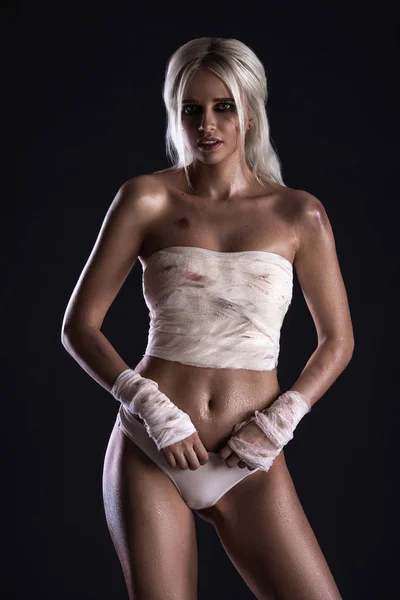 Beautiful young white-haired warrior girl with bandage on hands in light underwear on dark background