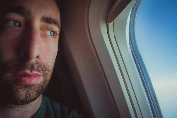 Close up of a pensive man looking outside through the window of an airplane.