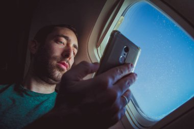 Onun smartphone vasıl seyir ve oturma pencere kenarındaki bir uçağın süre istimal o genç adam.