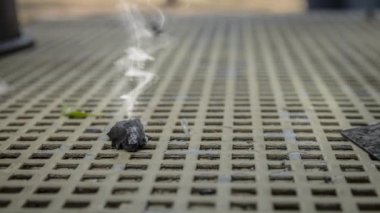 Metal bir masanın üzerindeki yanmış bir odun kömüründen yayılan duman sineması. Kapat, seçici odaklı döngü.