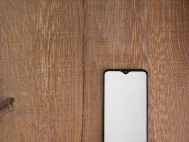 Yüzeyde, ahşap zemin üzerinde boş ekran izole edilmiş siyah mobil akıllı telefon modeli bulunuyor. En üstteki görünüm düzlüğü, ortasından kesilmiş kopyalama alanı ile yatıyordu.