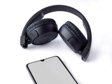 Beyaz arka planda siyah kablosuz kulaklık ve boş ekran maketli cep telefonu vardı. Üst görünüm seçici odaklanma ve kopyalama alanı ile yakın çekim. Müzik konsepti.