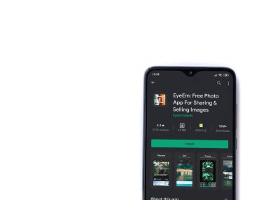 Lod, Israel - 8 Temmuz 2020: EyeEm - Resimleri Paylaşım ve Satma uygulamaları oyun mağazası sayfası beyaz arkaplanda izole edilmiş siyah bir cep telefonu ekranında. Üst görünüm düzlüğü kopyalama alanı ile yatıyordu.