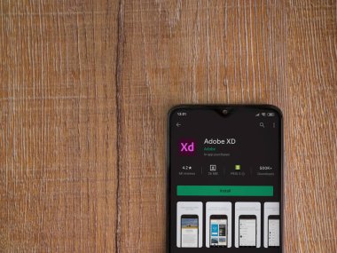 Lod, Israel - 8 Temmuz 2020: Adobe XD uygulaması oyun mağazası sayfası ahşap arka planda siyah bir cep telefonunun ekranında. Üst görünüm düzlüğü kopyalama alanı ile yatıyordu. 