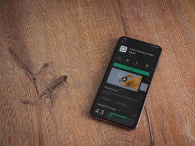 Lod, Israel - 8 Temmuz 2020: VSCO - Fotoğraf ve Video Editörü uygulama oyun sayfası ahşap arka planda siyah bir cep telefonunun ekranında. Üst görünüm düzlüğü kopyalama alanı ile yatıyordu. 