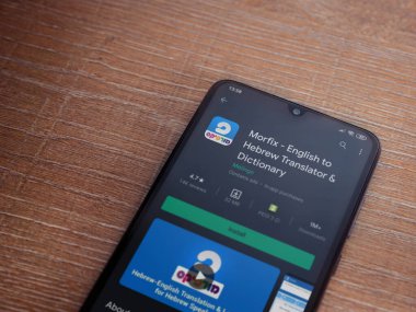 Lod, Israel - 8 Temmuz 2020: Morfix uygulaması oyun mağazası sayfası ahşap arka planda siyah bir cep telefonunun ekranında. Üst görünüm düzlüğü kopyalama alanı ile yatıyordu.