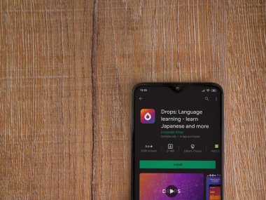 Lod, Israel - 8 Temmuz 2020: Damlalar - Dil öğrenme uygulaması oyun mağazası sayfası ahşap arka planda siyah bir cep telefonunun ekranında. Üst görünüm düzlüğü kopyalama alanı ile yatıyordu.