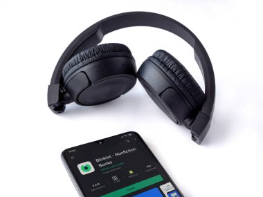 Lod, Israel - 8 Temmuz 2020: Blinkist uygulama oyun mağazası sayfası ve beyaz arka planda kablosuz kulaklıklı siyah cep telefonu. Üst görünüm düzlüğü kopyalama alanı ile yatıyordu.