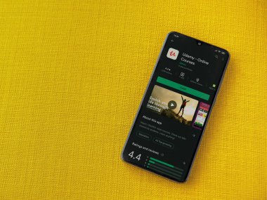 Lod, Israel - 8 Temmuz 2020: Udemy uygulaması oyun mağazası sayfası sarı kumaş arka planda siyah bir cep telefonunun ekranında. Üst görünüm düzlüğü kopyalama alanı ile yatıyordu.