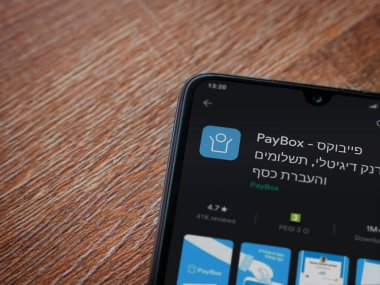 Lod, Israel - 8 Temmuz 2020: PayBox uygulaması oyun mağazası sayfası ahşap arka planda siyah bir cep telefonunun ekranında. Üst görünüm düzlüğü kopyalama alanı ile yatıyordu.