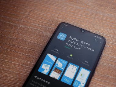 Lod, Israel - 8 Temmuz 2020: PayBox uygulaması oyun mağazası sayfası ahşap arka planda siyah bir cep telefonunun ekranında. Üst görünüm düzlüğü kopyalama alanı ile yatıyordu.