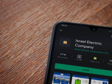 Lod, Israel - 8 Temmuz 2020: İsrail Elektrik Şirketi uygulama oyun mağazası sayfası ahşap arka planda siyah bir cep telefonunun ekranında. Üst görünüm düzlüğü kopyalama alanı ile yatıyordu.