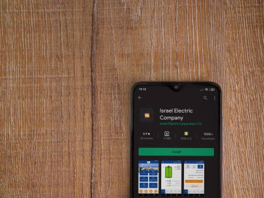 Lod, Israel - 8 Temmuz 2020: İsrail Elektrik Şirketi uygulama oyun mağazası sayfası ahşap arka planda siyah bir cep telefonunun ekranında. Üst görünüm düzlüğü kopyalama alanı ile yatıyordu.
