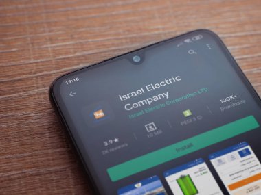 Lod, Israel - 8 Temmuz 2020: İsrail Elektrik Şirketi uygulama oyun mağazası sayfası ahşap arka planda siyah bir cep telefonunun ekranında. Üst görünüm düzlüğü kopyalama alanı ile yatıyordu.