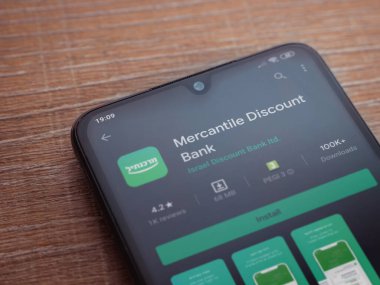 Lod, Israel - 8 Temmuz 2020: Bank Mercantil Discount uygulaması oyun mağazası sayfası ahşap arka planda siyah bir cep telefonu sergilenmektedir. Üst görünüm düzlüğü kopyalama alanı ile yatıyordu.
