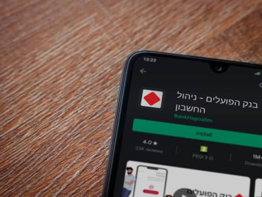 Lod, Israel - 8 Temmuz 2020: Bank Hapoalim uygulama oyun mağazası sayfası ahşap arka planda siyah bir cep telefonu görüntüsü. Üst görünüm düzlüğü kopyalama alanı ile yatıyordu.