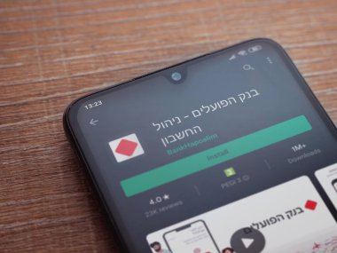 Lod, Israel - 8 Temmuz 2020: Bank Hapoalim uygulama oyun mağazası sayfası ahşap arka planda siyah bir cep telefonu görüntüsü. Üst görünüm düzlüğü kopyalama alanı ile yatıyordu.