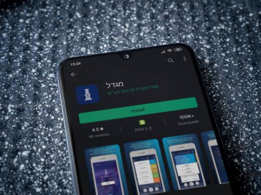 Lod, Israel - 8 Temmuz 2020: Metalik arka planda siyah bir cep telefonunun sergilendiği Migdal uygulaması oyun mağazası sayfası. Üst görünüm yatağını kapat.
