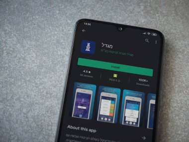 Lod, Israel - 8 Temmuz 2020: Migdal uygulaması oyun mağazası sayfası seramik taş zemin üzerinde siyah bir cep telefonu görüntüsü. Üst görünüm düzlüğü kopyalama alanı ile yatıyordu.