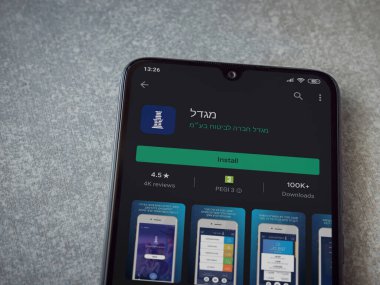 Lod, Israel - 8 Temmuz 2020: Migdal uygulaması oyun mağazası sayfası seramik taş zemin üzerinde siyah bir cep telefonu görüntüsü. Üst görünüm düzlüğü kopyalama alanı ile yatıyordu.