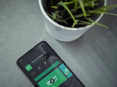 Lod, Israel - 8 Temmuz 2020: Mermer zemin üzerinde Bank Discount uygulaması oyun mağazası sayfası olan siyah cep telefonlu modern minimalist ofis çalışma alanı. Üst görünüm yatağını kapat.