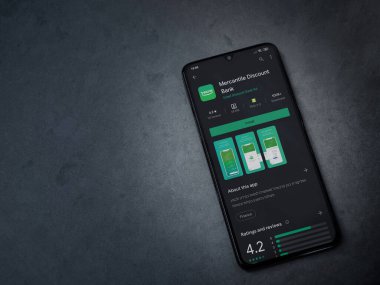 Lod, Israel - 8 Temmuz 2020: Bank Mercantil Discount uygulaması oyun mağazası sayfası koyu mermer taşlı arka planda siyah bir cep telefonu sergilenmektedir. Üst görünüm düzlüğü kopyalama alanı ile yatıyordu.