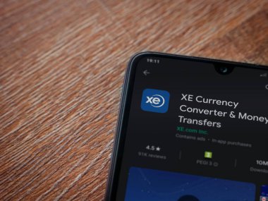 Lod, Israel - 8 Temmuz 2020: XE Para Birimi uygulaması oyun mağazası sayfası ahşap arka planda siyah bir cep telefonunun ekranında. Üst görünüm düzlüğü kopyalama alanı ile yatıyordu.