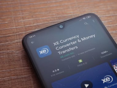 Lod, Israel - 8 Temmuz 2020: XE Para Birimi uygulaması oyun mağazası sayfası ahşap arka planda siyah bir cep telefonunun ekranında. Üst görünüm düzlüğü kopyalama alanı ile yatıyordu.