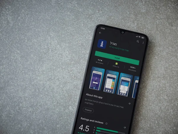 Lod, Israel - 8 Temmuz 2020: Migdal uygulaması oyun mağazası sayfası seramik taş zemin üzerinde siyah bir cep telefonu görüntüsü. Üst görünüm düzlüğü kopyalama alanı ile yatıyordu.
