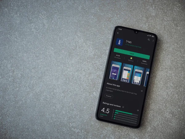 Lod, Israel - 8 Temmuz 2020: Migdal uygulaması oyun mağazası sayfası seramik taş zemin üzerinde siyah bir cep telefonu görüntüsü. Üst görünüm düzlüğü kopyalama alanı ile yatıyordu.