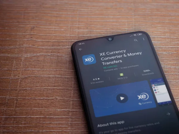 Lod, Israel - 8 Temmuz 2020: XE Para Birimi uygulaması oyun mağazası sayfası ahşap arka planda siyah bir cep telefonunun ekranında. Üst görünüm düzlüğü kopyalama alanı ile yatıyordu.