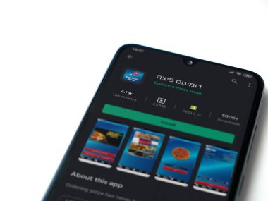 Lod, Israel - 8 Temmuz 2020: Domino 'nun Pizza Israel uygulaması oyun mağazası sayfası beyaz arka planda izole edilmiş siyah bir cep telefonunun ekranında. Üst görünüm düzlüğü kopyalama alanı ile yatıyordu.