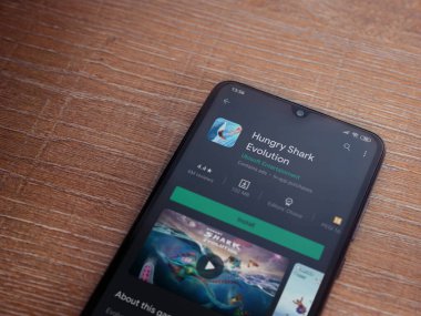 Lod, Israel - 8 Temmuz 2020: Aç Köpekbalığı Evrim uygulaması oyun mağazası sayfası ahşap arka planda siyah bir cep telefonunun ekranında. Üst görünüm düzlüğü kopyalama alanı ile yatıyordu.