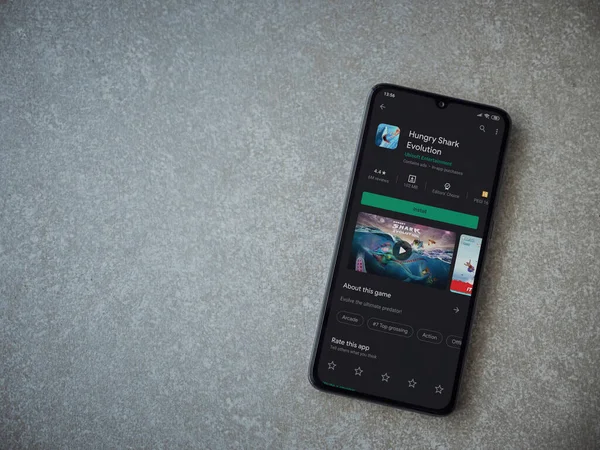 Lod, Israel - 8 Temmuz 2020: Hungry Shark Evolution uygulama oyun mağazası sayfası seramik taş zemin üzerinde siyah bir cep telefonu görüntüsü. Üst görünüm düzlüğü kopyalama alanı ile yatıyordu.