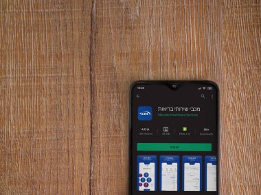 Lod, Israel - 8 Temmuz 2020: Maccbi Sağlık Hizmetleri uygulama oyun mağazası sayfası ahşap arka planda siyah bir cep telefonu sergilenmektedir. Üst görünüm düzlüğü kopyalama alanı ile yatıyordu.