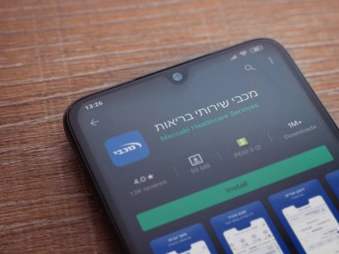 Lod, Israel - 8 Temmuz 2020: Maccbi Sağlık Hizmetleri uygulama oyun mağazası sayfası ahşap arka planda siyah bir cep telefonu sergilenmektedir. Üst görünüm düzlüğü kopyalama alanı ile yatıyordu.