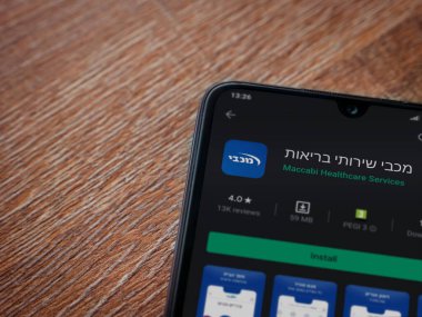 Lod, Israel - 8 Temmuz 2020: Maccbi Sağlık Hizmetleri uygulama oyun mağazası sayfası ahşap arka planda siyah bir cep telefonu sergilenmektedir. Üst görünüm düzlüğü kopyalama alanı ile yatıyordu.