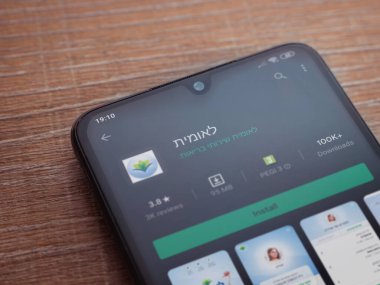 Lod, Israel - 8 Temmuz 2020: Leumit Health Services uygulama oyun mağazası sayfası ahşap arka planda siyah bir cep telefonu sergilenmektedir. Üst görünüm düzlüğü kopyalama alanı ile yatıyordu.
