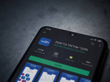 Lod, Israel - 8 Temmuz 2020: Maccbi Sağlık Hizmetleri uygulama oyun mağazası sayfası koyu mermer taşlı arka planda siyah bir cep telefonu sergilenmektedir. Üst görünüm düzlüğü kopyalama alanı ile yatıyordu.