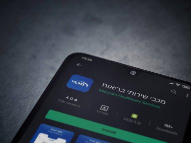Lod, Israel - 8 Temmuz 2020: Maccbi Sağlık Hizmetleri uygulama oyun mağazası sayfası koyu mermer taşlı arka planda siyah bir cep telefonu sergilenmektedir. Üst görünüm düzlüğü kopyalama alanı ile yatıyordu.