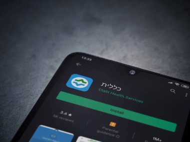 Lod, Israel - 8 Temmuz 2020: Clalit Sağlık Hizmetleri uygulama oyun mağazası sayfası koyu mermer taşlı arka planda siyah bir cep telefonu sergilenmektedir. Üst görünüm düzlüğü kopyalama alanı ile yatıyordu.