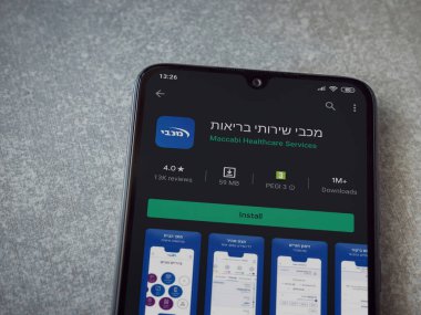 Lod, Israel - 8 Temmuz 2020: Maccbi Sağlık Hizmetleri uygulama oyun mağazası sayfası seramik taş zemin üzerinde siyah bir cep telefonu görüntüsü. Üst görünüm düzlüğü kopyalama alanı ile yatıyordu.