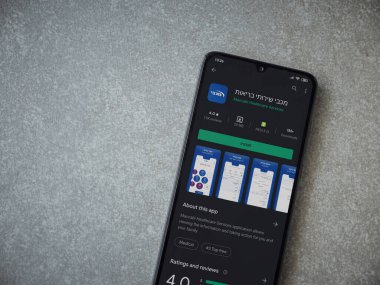 Lod, Israel - 8 Temmuz 2020: Maccbi Sağlık Hizmetleri uygulama oyun mağazası sayfası seramik taş zemin üzerinde siyah bir cep telefonu görüntüsü. Üst görünüm düzlüğü kopyalama alanı ile yatıyordu.