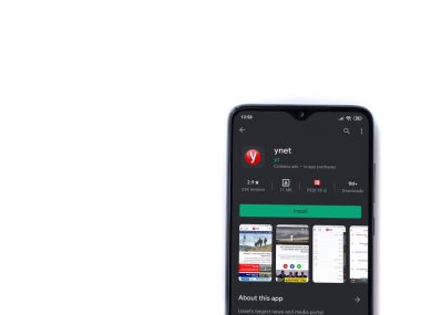 Lod, Israel - 8 Temmuz 2020: ynet uygulama oyun mağazası sayfası beyaz arkaplanda izole edilmiş siyah bir cep telefonu ekranında. Üst görünüm düzlüğü kopyalama alanı ile yatıyordu.