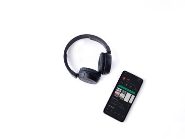 Lod, Israel - 8 Temmuz 2020: Ynet uygulamalı akıllı telefon oyun mağazası sayfası ve beyaz arka planda kablosuz kulaklıklar. Üst görünüm düzlüğü kopyalama alanı ile yatıyordu.