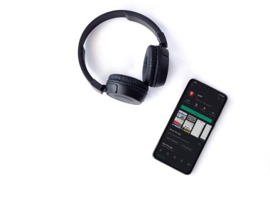 Lod, Israel - 8 Temmuz 2020: Ynet uygulamalı akıllı telefon oyun mağazası sayfası ve beyaz arka planda kablosuz kulaklıklar. Üst görünüm düzlüğü kopyalama alanı ile yatıyordu.