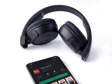 Lod, Israel - 8 Temmuz 2020: N12 uygulama oyun mağazası sayfası ve beyaz arka planda kablosuz kulaklığı olan siyah cep telefonu. Üst görünüm düzlüğü kopyalama alanı ile yatıyordu.