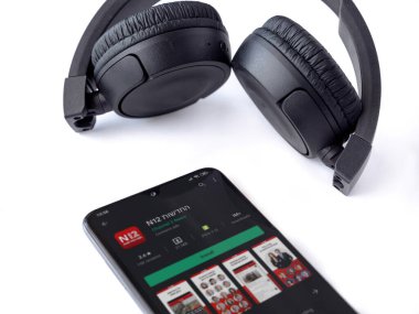 Lod, Israel - 8 Temmuz 2020: N12 uygulama oyun mağazası sayfası ve beyaz arka planda kablosuz kulaklığı olan siyah cep telefonu. Üst görünüm düzlüğü kopyalama alanı ile yatıyordu.