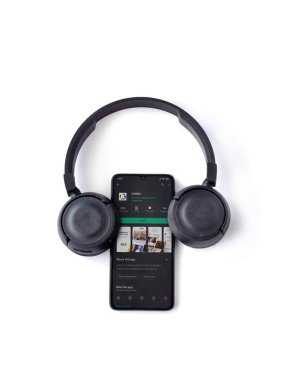 Lod, Israel - 8 Temmuz 2020: Mako app oyun mağazası sayfası ve beyaz arka planda kablosuz kulaklıkları olan siyah cep telefonu. Üst görünüm düzlüğü kopyalama alanı ile yatıyordu.