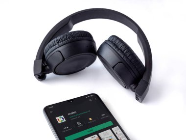 Lod, Israel - 8 Temmuz 2020: Mako app oyun mağazası sayfası ve beyaz arka planda kablosuz kulaklıkları olan siyah cep telefonu. Üst görünüm düzlüğü kopyalama alanı ile yatıyordu.